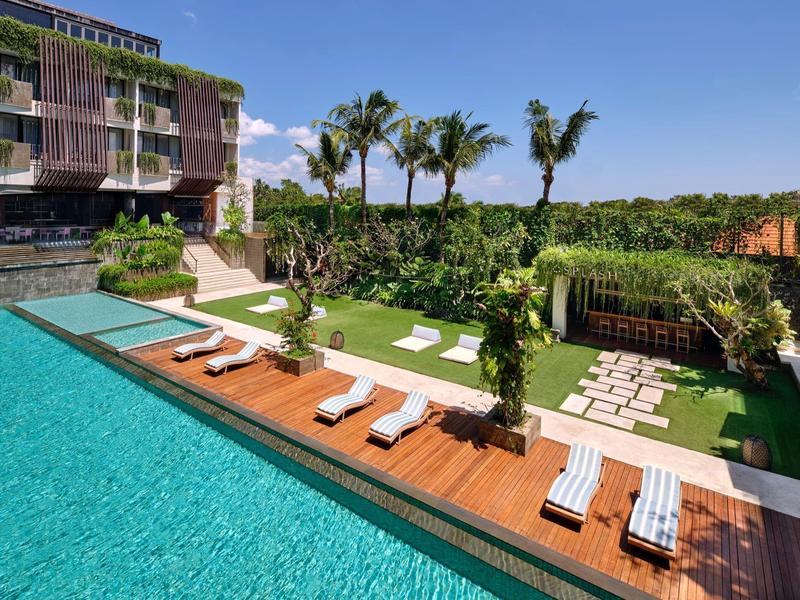 Nowoczesny basen na zewnątrz z leżakami i palmami obok budynku hotelowego.