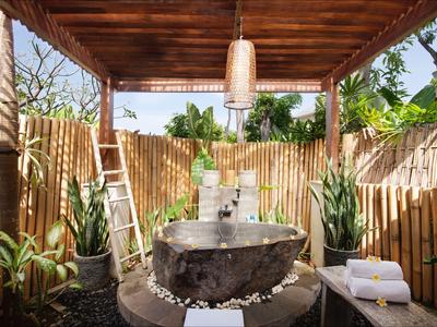 Espace douche en plein air avec baignoire en pierre, clôture en bambou et plantes tropicales.