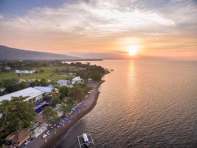 Sunset over calm sea with beach, hotel, and hills in the background