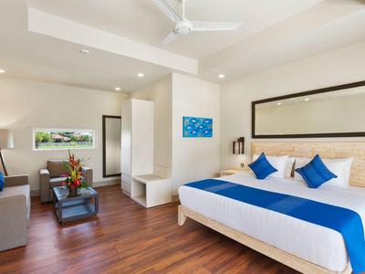 Modern hotel room with king-size bed, blue and white bedding, sofa, and wooden flooring.