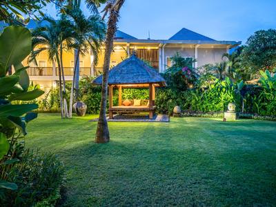 Garden with lawn, palm trees, and wooden pavilion at dusk in a hotel.