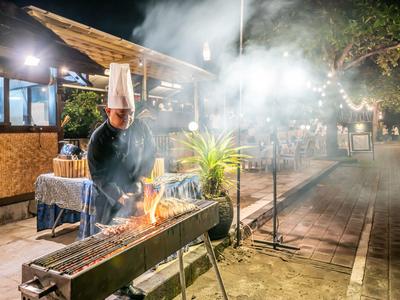 Chef portant un chapeau blanc grillant avec des flammes et de la fumée en plein air la nuit près d'un restaurant