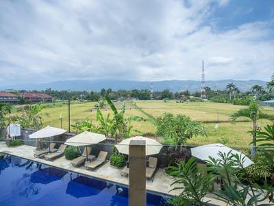 Hotel pool with lounge chairs overlooking green rice fields under a cloudy sky.