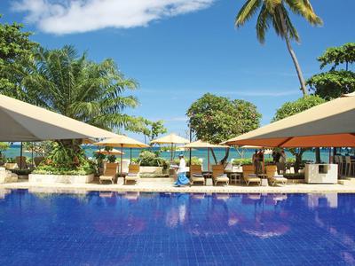 Blue pool with sun umbrellas, lounge chairs, and palm trees on the beach