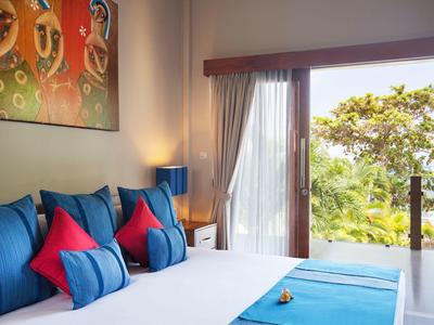 Bright hotel room with blue and red pillows, wall art, and garden view.