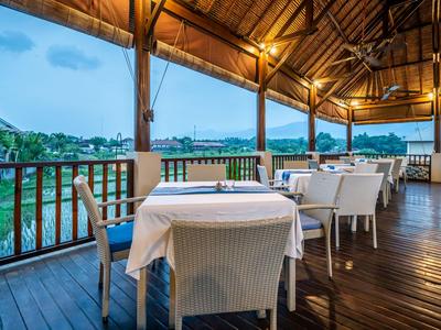 Terrasse couverte avec tables dressées surplombant l'eau et les collines au coucher du soleil.