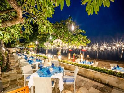 Evening terrace with set tables, surrounded by lit trees next to a beach.