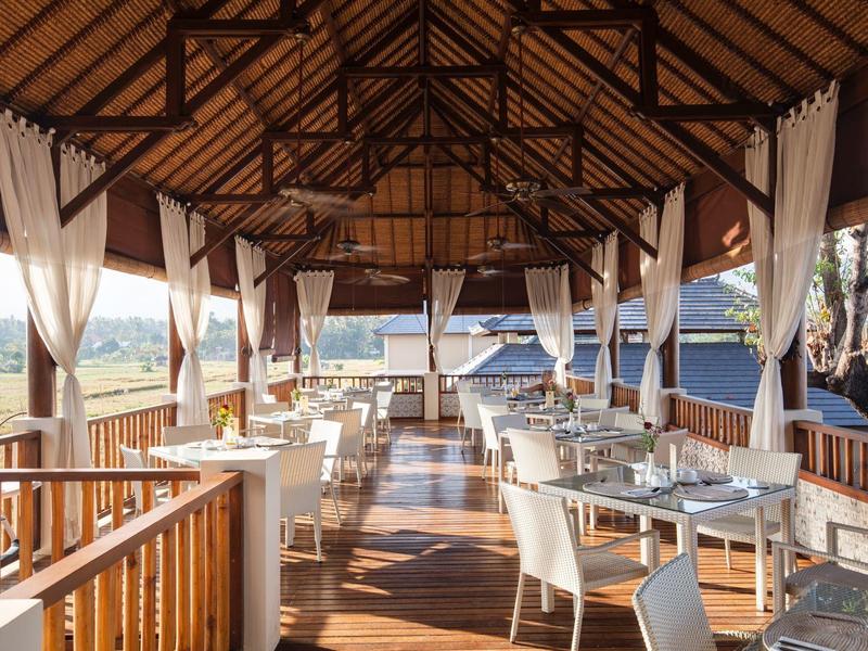 Open dining area under wooden pitched roof with nature view and elegantly set tables.