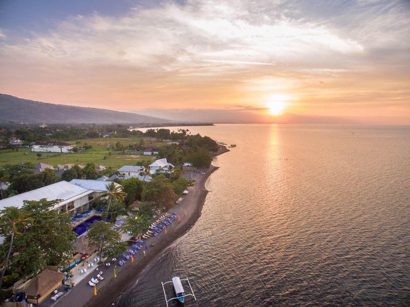 Sunset over calm sea with beach, hotel, and hills in the background