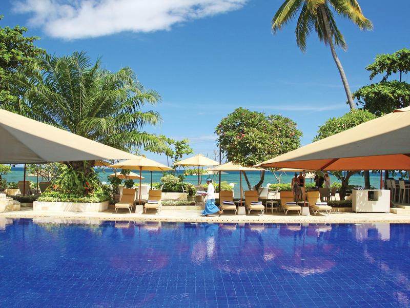 Blue pool with sun umbrellas, lounge chairs, and palm trees on the beach