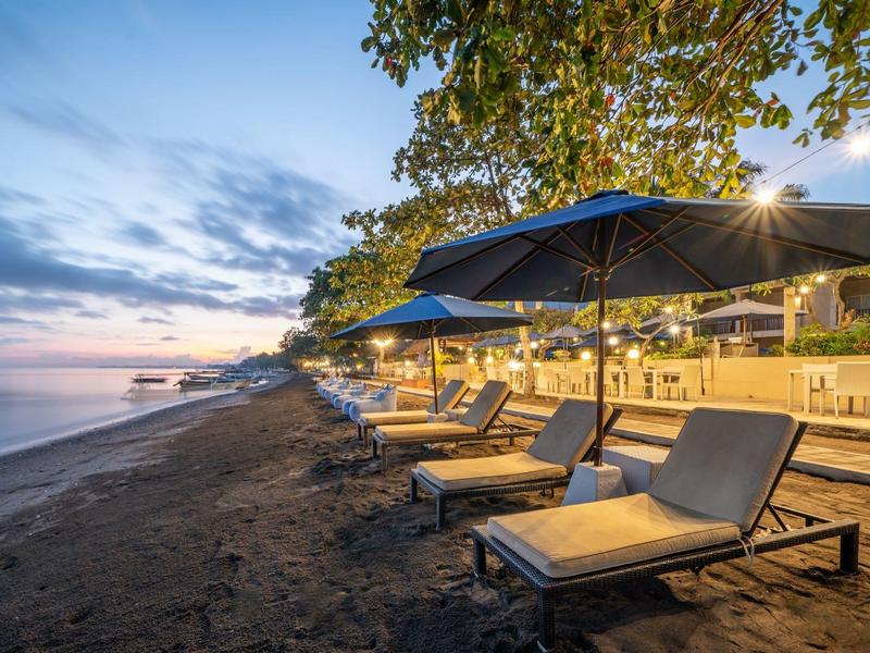 Empty lounge chairs with umbrellas on a sandy beach at sunset.