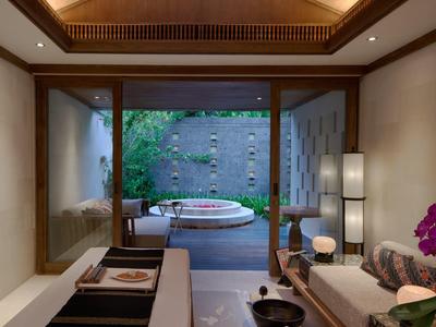 Chambre d'hôtel luxueuse donnant sur un jardin privé et un jacuzzi sous un plafond en bois.