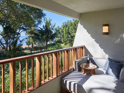 Coin salon confortable sur balcon avec lit de jour, coussins et vue sur arbres tropicaux et mer.
