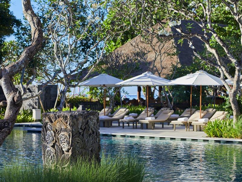 Une piscine luxueuse avec des chaises longues et des parasols entourée d'arbres.