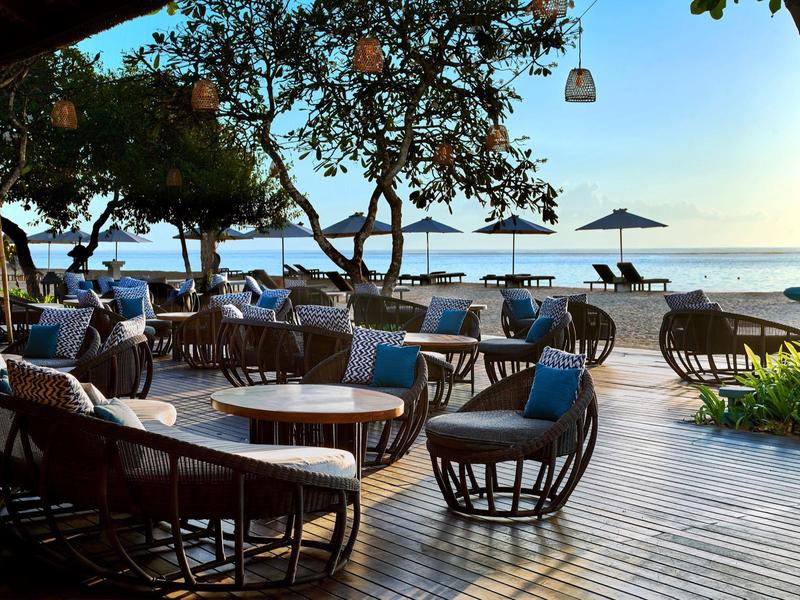 Terrasse ouverte avec tables et chaises sur la plage avec vue sur le coucher de soleil et la mer.