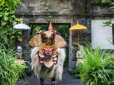 Traditional Asian mask and costume in front of a temple decorated with plants