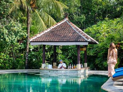 A pool with a covered seating area in a tropical garden.