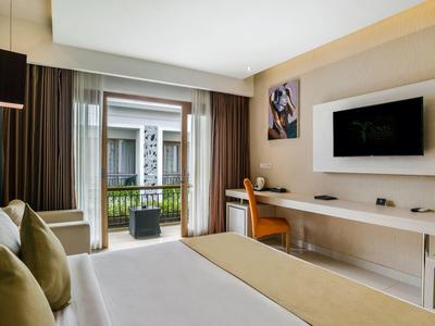 Nowoczesny pokój hotelowy z dużym łóżkiem, biurkiem i balkonem z widokiem na inne budynki.