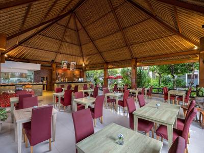 Restauracja na świeżym powietrzu z drewnianym dachem, czerwonymi krzesłami i zielonym widokiem na zewnątrz.