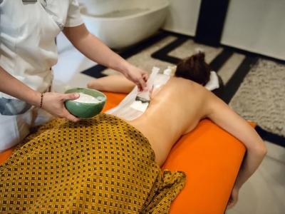 Osoba otrzymująca masaż pleców z ciepłym olejem w pokoju hotelowym spa.