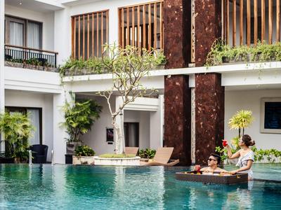 Two people relax on a floating tray in a hotel pool with modern architecture.