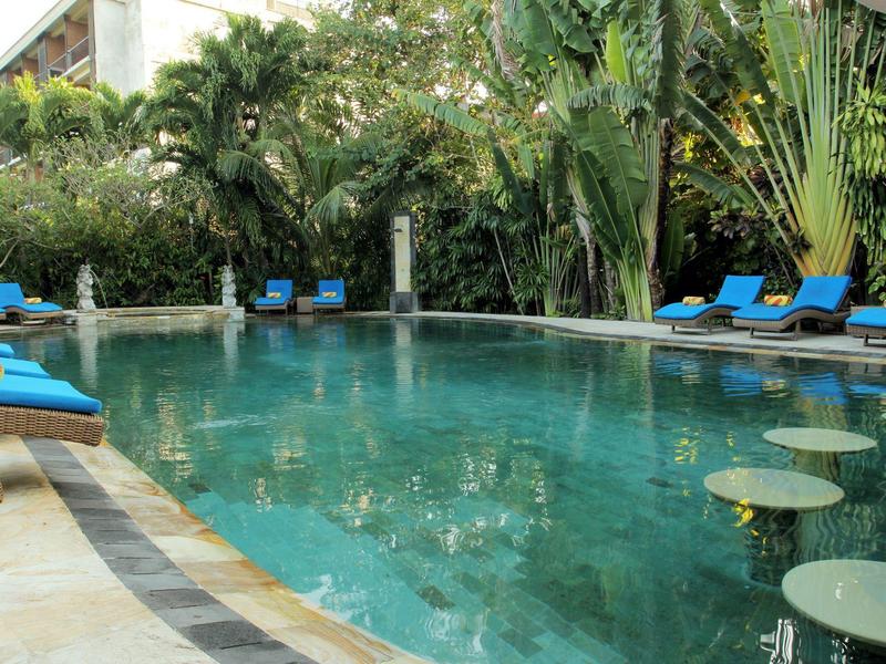 Piękny basen z wysokimi palmami i niebieskimi leżakami w tropikalnym hotelu.