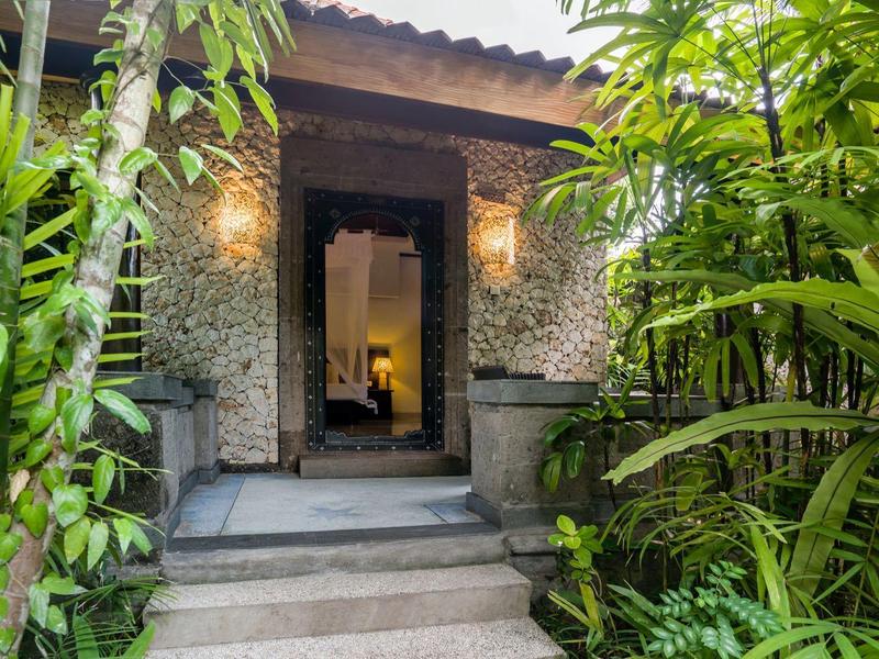 Wejście do pokoju hotelowego z ciepłym oświetleniem i bujną zieloną roślinnością.