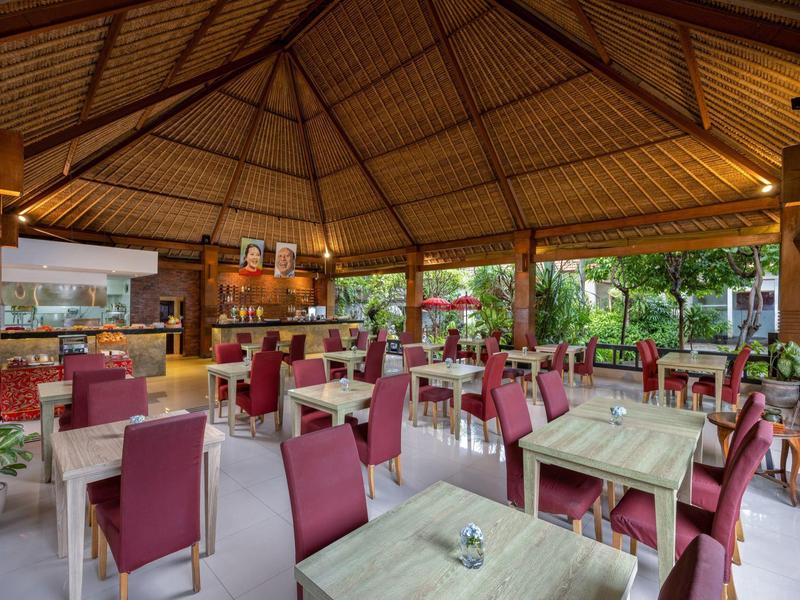 Restauracja na świeżym powietrzu z drewnianym dachem, czerwonymi krzesłami i zielonym widokiem na zewnątrz.