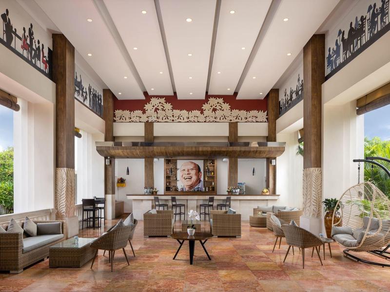 Przestronna lobby hotelowa z wysokimi sufitami, miejscami do siedzenia i barem w tle.