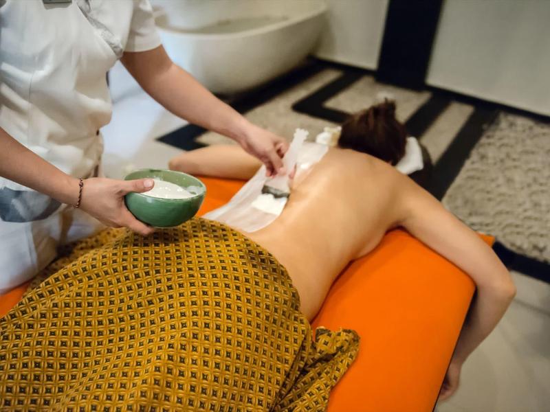 Osoba otrzymująca masaż pleców z ciepłym olejem w pokoju hotelowym spa.