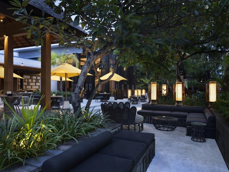 Zona exterior de hotel con asientos, faroles iluminados y árboles al anochecer.