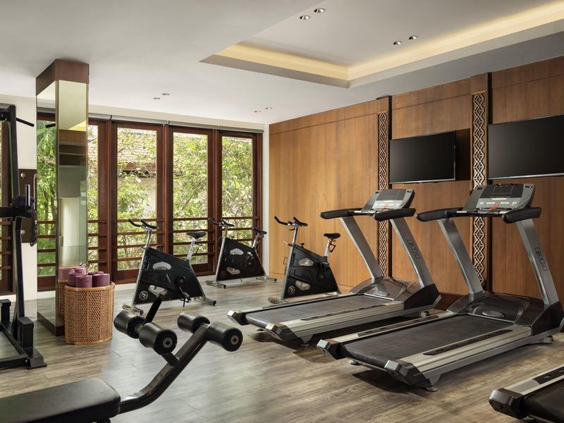Gimnasio moderno con cintas de correr y máquinas de cardio junto a grandes ventanas con vista al jardín.