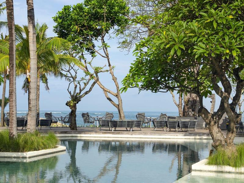 Piscina tranquila rodeada de árboles con vista al océano bajo un cielo despejado.