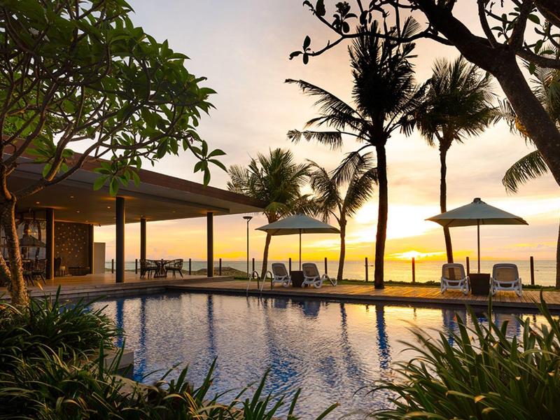 Área de piscina con tumbonas y palmeras al atardecer en un resort tropical.