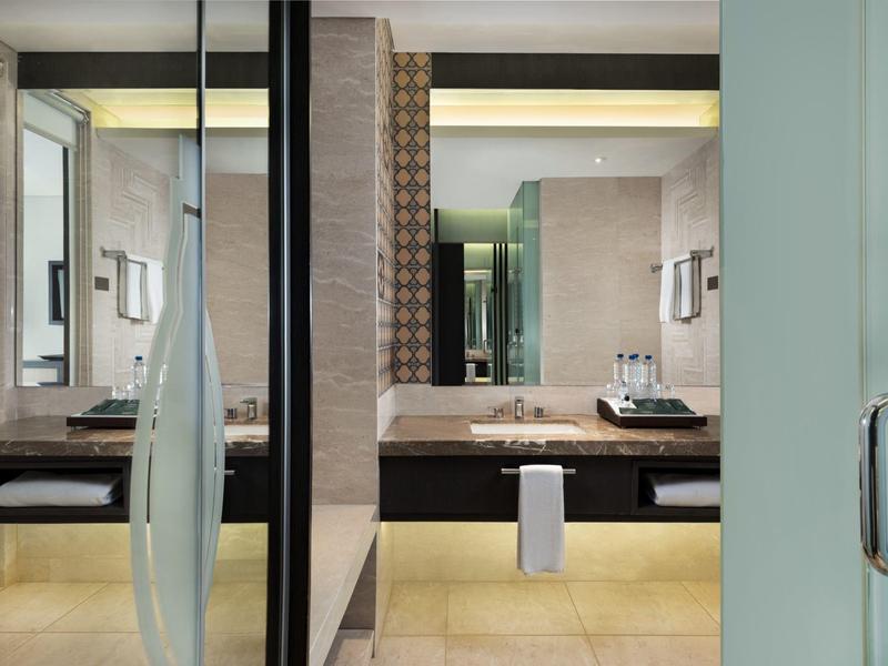 Área moderna de baño con lavabo, espejos y toallas en ambiente claro.