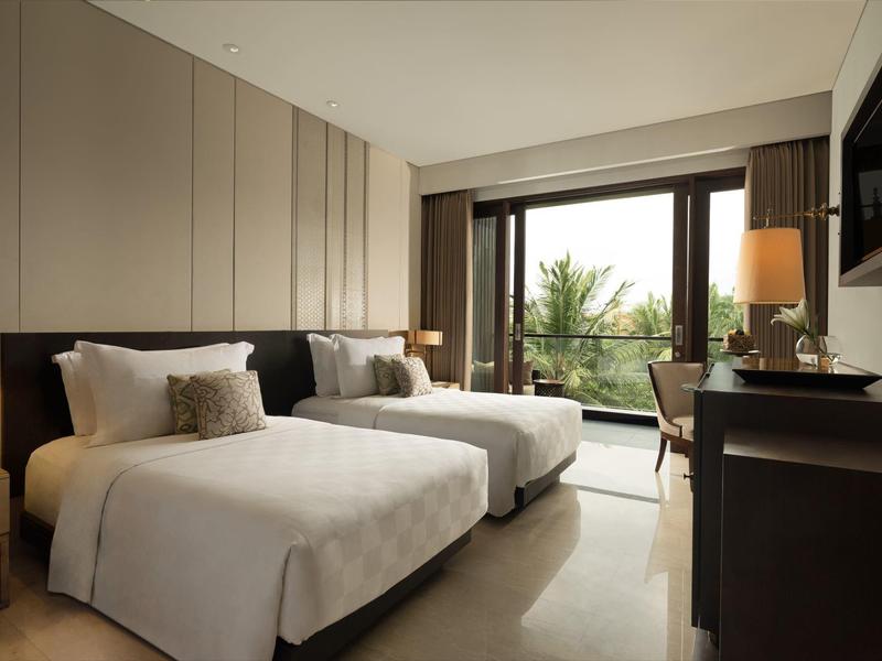 Habitación de hotel moderna con dos camas, decoración clara y vista a palmeras por grandes ventanas.