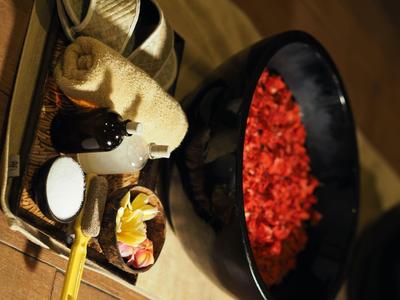 Ciotola nera con petali rossi, asciugamano beige, cucchiaio, candela e accessori spa su vassoio.