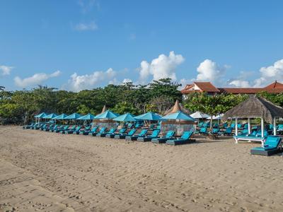 Spiaggia con ombrelloni blu e lettini davanti a un hotel sotto un cielo soleggiato.