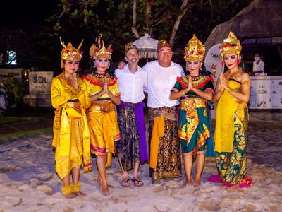 Due uomini posano con quattro donne vestite in abiti tradizionali davanti a uno sfondo tropicale di notte.