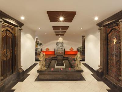 Ingresso d'hotel con statue asiatiche, sedili rossi, pareti bianche e illuminazione soffusa.