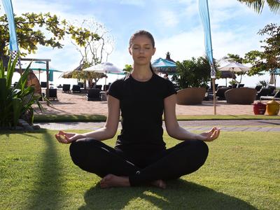Persona che medita in posizione del loto sull'erba verde con vista sulla spiaggia e sul mare.