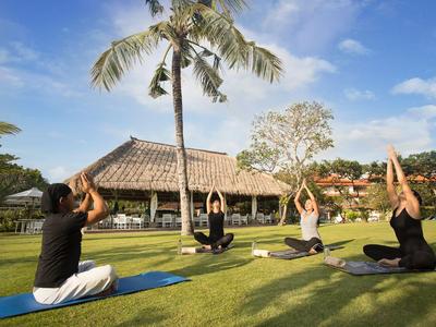 Gruppo che pratica yoga sull'erba con palme e edificio in stile asiatico sullo sfondo.