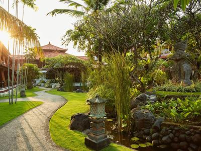 Giardino tropicale soleggiato dell'hotel con sentiero curato, palme e vegetazione rigogliosa.