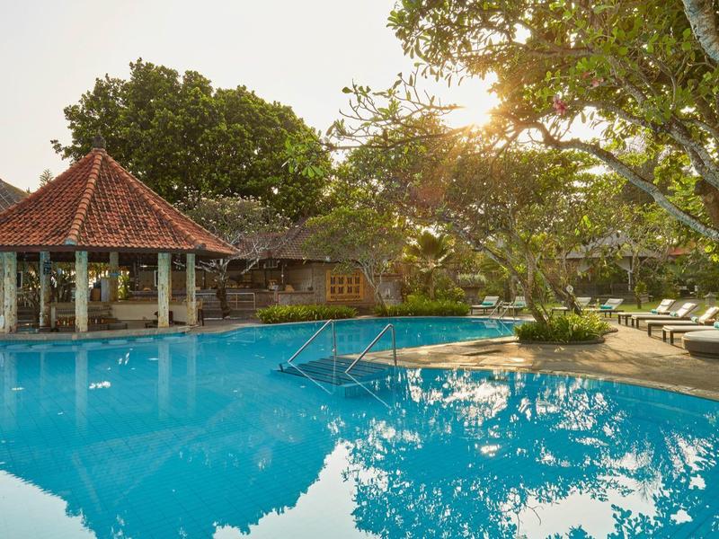 Piscina a sfioro con bar interno, circondata da vegetazione e lettini al tramonto.
