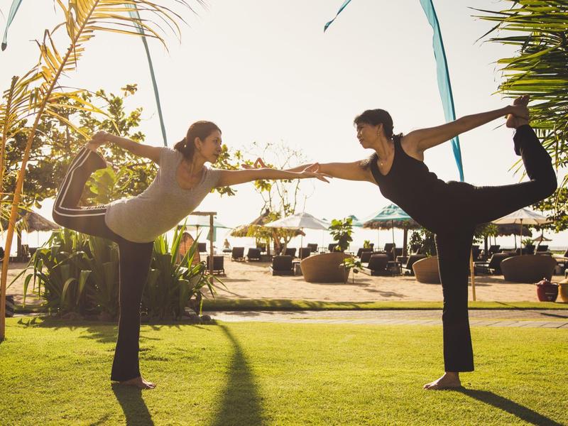 Due donne fanno yoga in equilibrio in un giardino soleggiato vicino alla spiaggia.