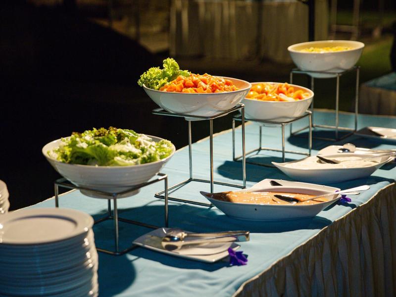 Buffet di insalate fresche in ciotole bianche su tavolo blu.