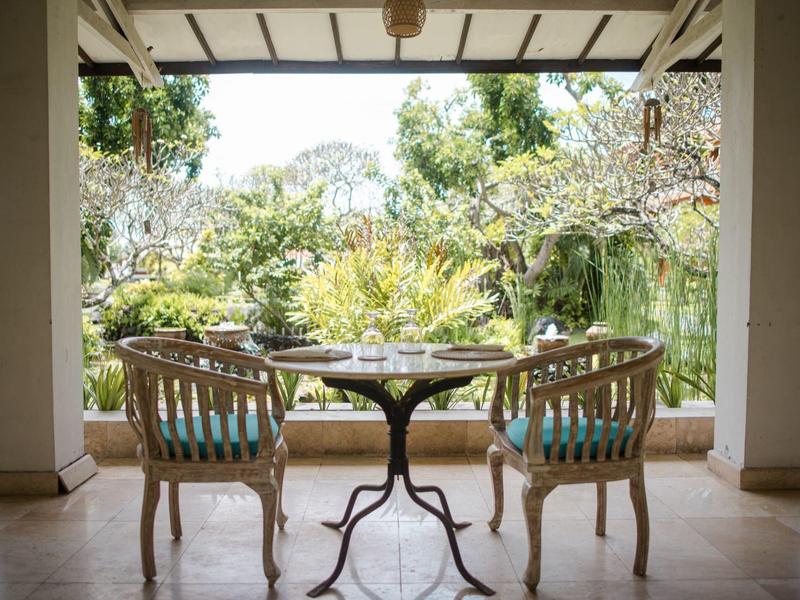 Terrazza coperta con sedie e tavolo, vista su giardino verdeggiante.