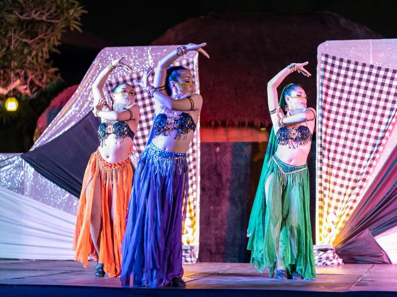 Tre ballerine con costumi colorati eseguono una danza sul palco decorato per uno spettacolo.