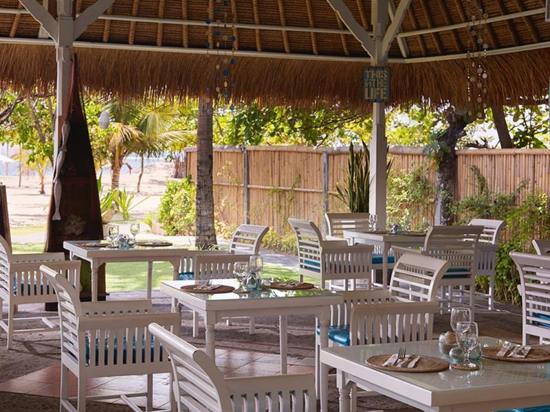 Terrazza ombreggiata con tavoli di legno bianchi e vista sul giardino.