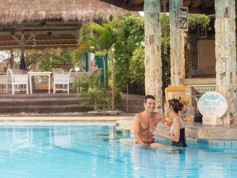 Coppia a bordo piscina in un hotel tropicale con arredi bianchi e vegetazione rigogliosa.